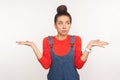 Maybe, don`t know! Portrait of clueless confused girl with hair bun in denim overalls having doubts, not sure about decision Royalty Free Stock Photo