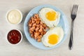 Mayonnaise and ketchup, plate with fried eggs and pieces of sausage, fork on wooden table. Top view