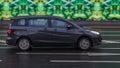 Mazda Premacy Third generation CW on wet city road. Dark gray compact minivan with man driving. Mazda5 auto in fast motion with