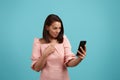 Me. Surprised woman with dark hair in pink dress is looking at her mobile phone screen, cannot believe news, keeps mouth Royalty Free Stock Photo