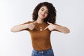 Me who you need. Self-assured attractive cheerful curly-haired glad girl bragging pointing herself chest smiling Royalty Free Stock Photo