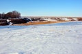 Meadow covered with snow, line of yellow dry reeds on other hill, trees on horizon, winter landscape, blue sky