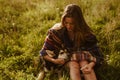 on the meadow grass sits a girl in an ethno cape and strokes the dog gently hugging her hand Royalty Free Stock Photo