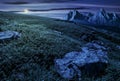 Meadow with huge stones on top of mountain range at night