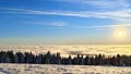 The meadow on the mountain plateau is covered with snow. Below is a snow-covered spruce forest, shrouded in clouds and fog. Above Royalty Free Stock Photo