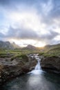 A meadow on top of a mountain, surrounded by rocky peaks, with a small river ending in a small waterfall in the foreground, cows Royalty Free Stock Photo