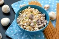 Meal from pasta spaghetti, mushroom, cottage cheese and parsley in blue bowl on dot cloth on black background