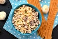 Meal from pasta spaghetti, mushroom, cottage cheese and parsley in blue bowl on dot cloth on black background