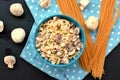 Meal from pasta spaghetti, mushroom, cottage cheese and parsley in blue bowl on dot cloth on black background