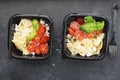 Meal prep. Black lunch boxes. Pasta bows, cherry tomatoes, young cheese, salt, pepper, basil. On a dark background. Top Royalty Free Stock Photo