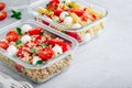 Meal prep containers with pasta salad or quinoa, tomatoes, mozzarella cheese, and basil