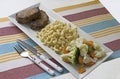 Meal serving consisting of steak and macaroni and veggies on an oblong white plate.
