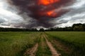 Dirt road through green field and dark stormy sky with clouds Royalty Free Stock Photo