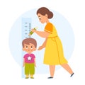 Measuring height. Mom helps her son measure growth, makes mark with pencil, wall-mounted kids meter, little boy standing