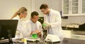 Measuring solutions and recording data at lab bench, chemists in lab coats and goggles with flasks Royalty Free Stock Photo