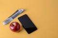 Measuring tape with centimeters, smartphone and ripe red apple on a textured yellow background. Concept of healthy eating, dieting Royalty Free Stock Photo