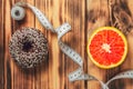 Measuring tape dividing wooden surface between chocolate donut and orange, choice between healthy and unhealthy food Royalty Free Stock Photo