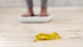 Measuring tape lying on floor and blurred view of young woman standing on scales, checking her weight, selective focus Royalty Free Stock Photo
