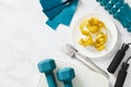 Measuring tape on plate with cutlery, scales, jump rope, roller, elastic band, dumbbells on marble table. Weight loss concept Royalty Free Stock Photo