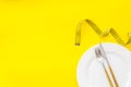 Measuring tape, plate with fork and knife on yellow background top view mockup Royalty Free Stock Photo