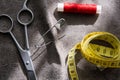 Measuring tape, scissors and reel of red thread on gray fabric Royalty Free Stock Photo