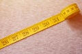 The measuring tape of yellow color with numerical indicators in the form of centimeters or inches lies on a gray knitted fabric. Royalty Free Stock Photo