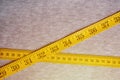 The measuring tape of yellow color with numerical indicators in the form of centimeters or inches lies on a gray knitted fabric. Royalty Free Stock Photo