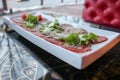 Meat appetizer of red beef and pork sprinkled with cheese and greens on a white rectangular plate on a table in a cafe Royalty Free Stock Photo