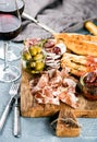 Meat appetizer selection. Salami, prosciutto, bread sticks, baguette, olives and sun-dried tomatoes, two glasses of red