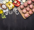 Meat balls with herbs and onions on a cutting board with vegetables, spices, oil, vintage wooden spoon on wooden rustic background