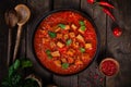 Meat beef pieces in pan with tomato sauce, vegetables, wooden background