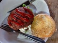 Meat buger on a dish. topped with tomato sauce with knife and fork.