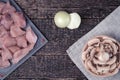 Meat cut into pieces, peeled onion and a bowl of chopped champignons on an old wood texture background