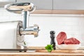 Meat grinder with fresh meat on a wooden table in kitchen interior