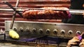 The meat of the ribs rotates on the grill in the diner. A cook in gloves is preparing a new serving on the barbecue. Grilled food
