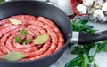 Meat sausages in frying pan, with bay leaves and fresh herbs in the kitchen Royalty Free Stock Photo