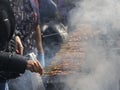 Meat skewers on barbecue grill with smoke and hands