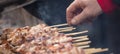 Meat skewers souvlaki on grill. Man`s hand ready to touch the skewers, front view, close up, banner. Royalty Free Stock Photo