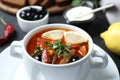 Meat solyanka soup with sausages, olives and vegetables in bowl on table, closeup