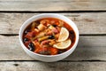 Meat solyanka soup with sausages, olives and vegetables in bowl on wooden table