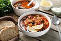 Meat solyanka soup with sausages, olives and vegetables served on wooden table