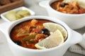 Meat solyanka soup with sausages, olives and vegetables on white table, closeup