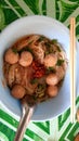 Meatball noodles with small white strips Served with garnish and vegetables. There are eating utensils, chopsticks and spoons.