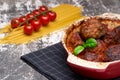 Meatballs with cherry tomato sauce and decorated with basil leaf, served in white and red pan on grey background. next to the pan Royalty Free Stock Photo