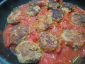 Meatballs frying in a tomato sauce in a hot pan