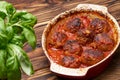 Meatballs in tomato sauce in a baking bowl, wooden table. View from above. basil in the foreground in defocus. baked meatballs Royalty Free Stock Photo