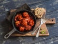 Meatballs in tomato sauce in a pan on rustic wooden cutting board