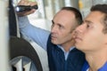 Mechanic and apprentice working on car together