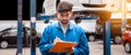 Mechanic in blue work wear uniform checks the vehicle maintenance checklist with blur lifted car in the background.