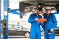 Mechanic in blue work wear uniform inspects the car bottom with his assistant. Automobile repairing service, Royalty Free Stock Photo